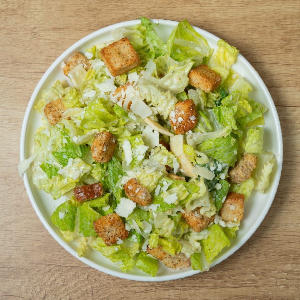 Overhead view of a Caesar salad with romaine lettuce, croutons, and parmesan cheese on a white plate.