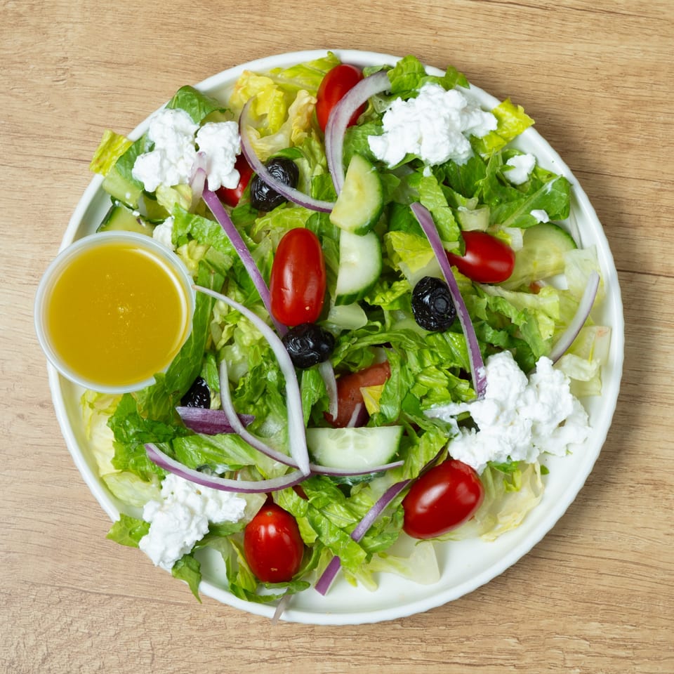 Fresh garden salad with lettuce, tomatoes, cucumbers, red onions, black olives, feta cheese, and dressing.