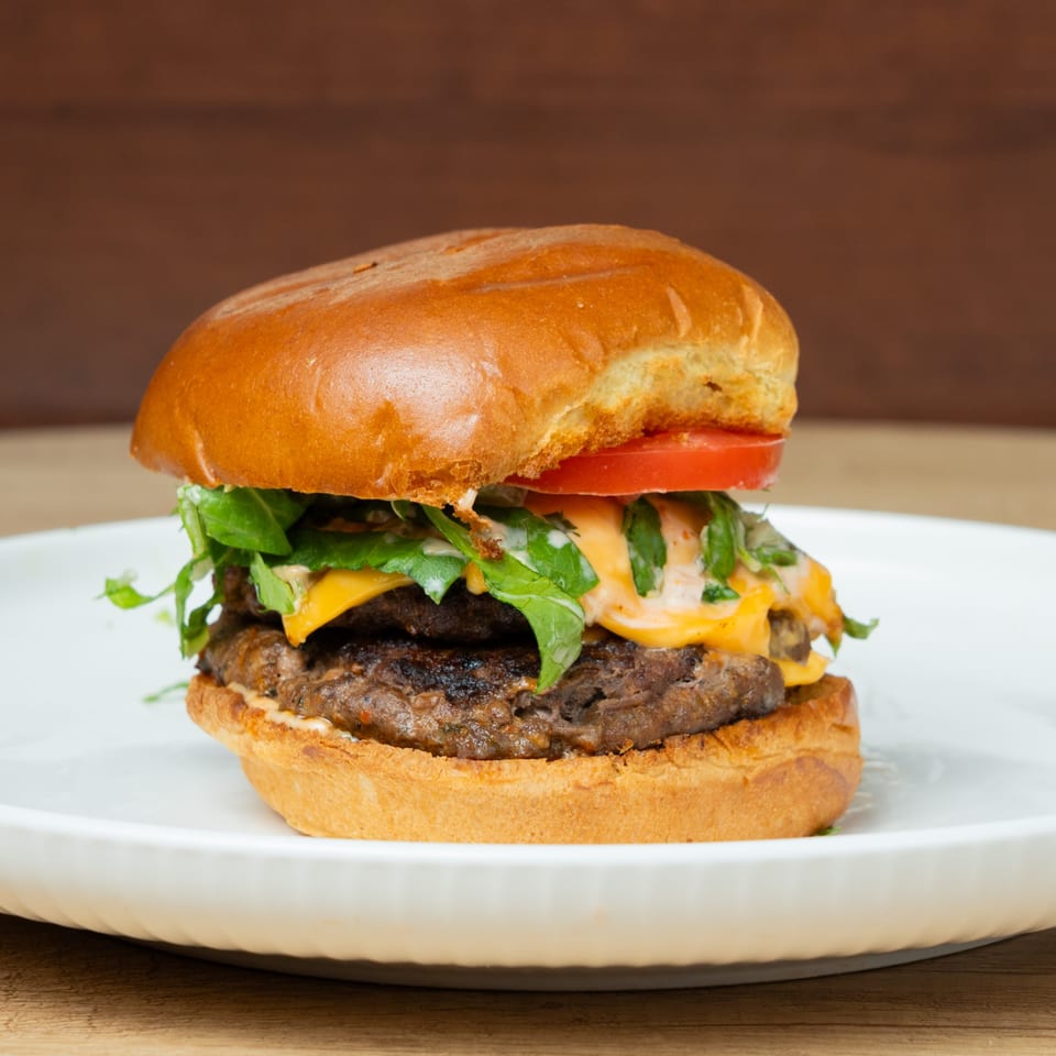 A double cheeseburger with melted cheese, lettuce, tomato, and sauce on a brioche bun.