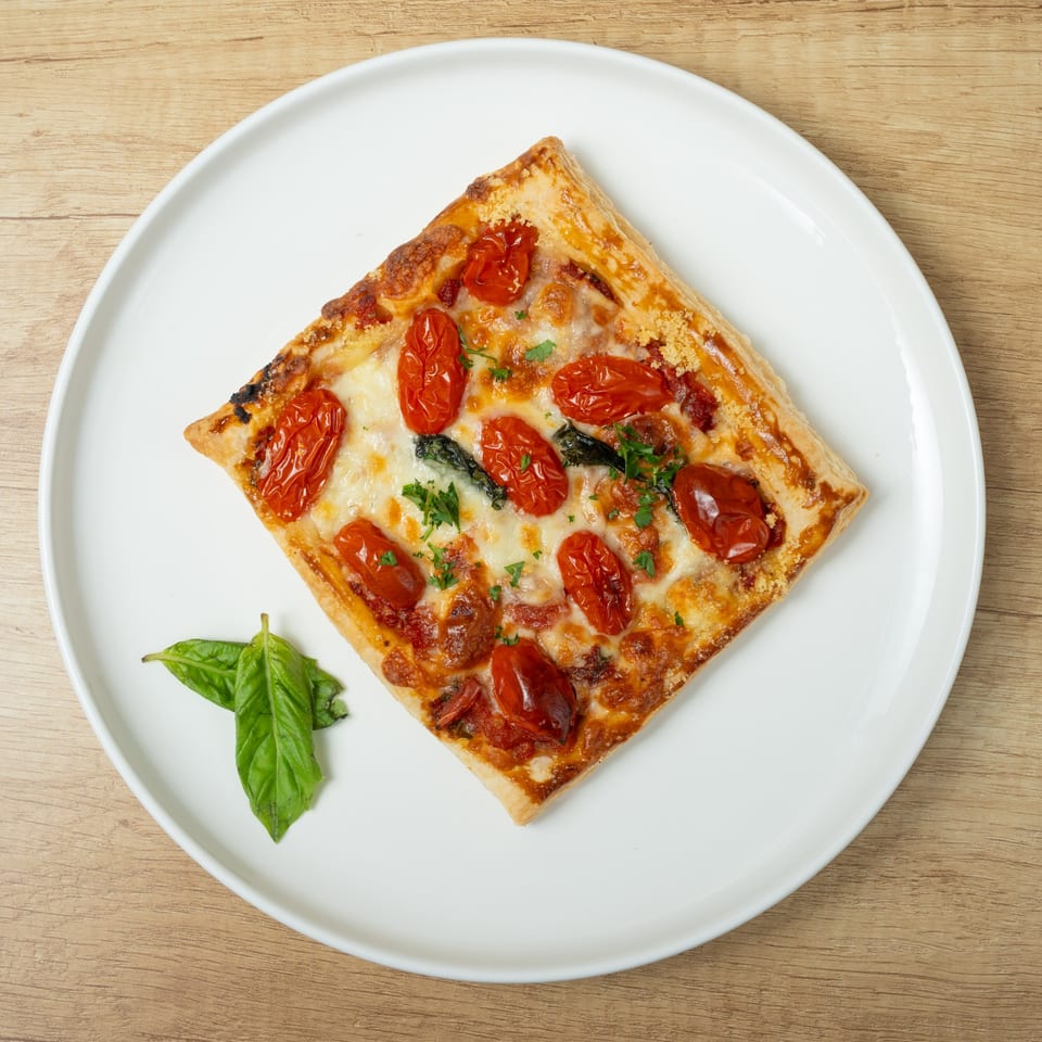 Square flatbread pizza with roasted cherry tomatoes, melted cheese, and fresh basil on a white plate.
