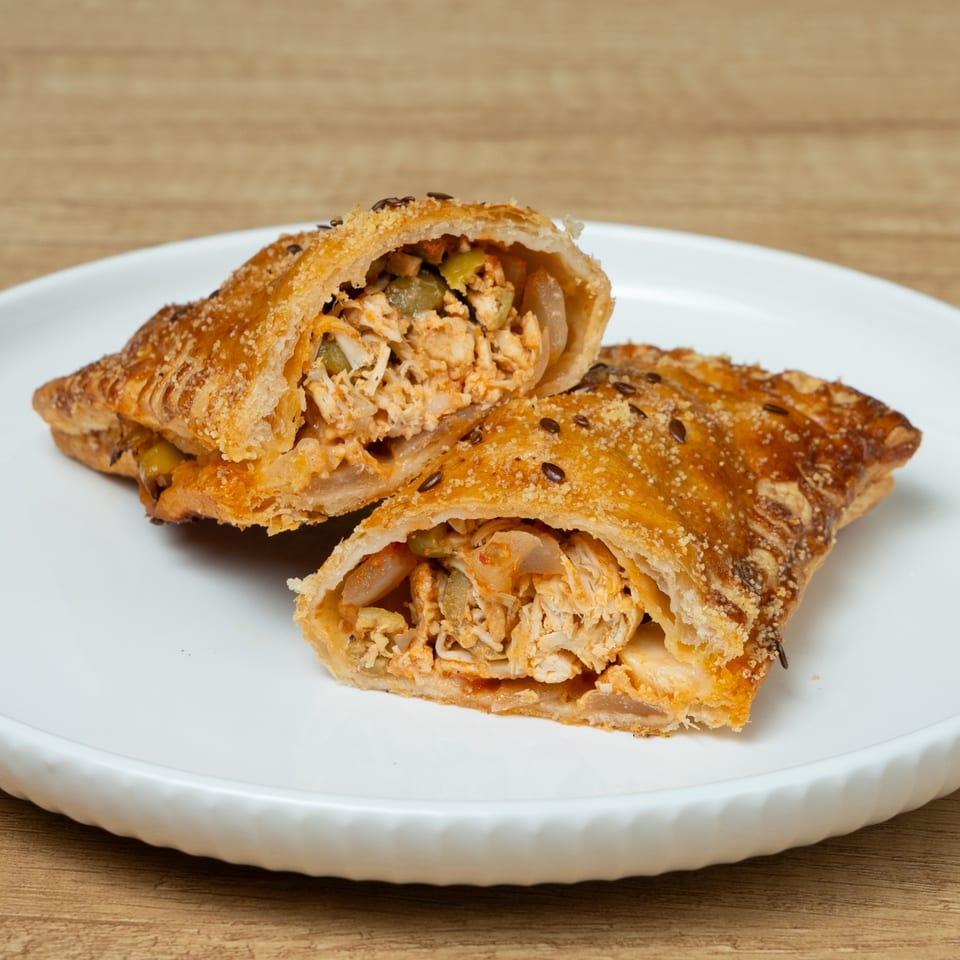 Two golden-brown pastries, cut open to reveal a savory chicken and vegetable filling, on a white plate.